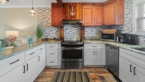A modern kitchen with wooden cabinets, a stainless steel stove, and a tiled backsplash. - 7904 Surf Dr #7 (Panama City Beach)