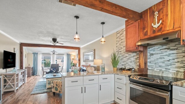 A modern kitchen with white cabinets, a stainless steel oven, and a wooden ceiling. - 7904 Surf Dr #7 (Panama City Beach)