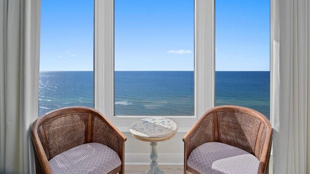 A room with two wicker chairs facing a large window overlooking the ocean. - Emerald Beach 2325 (Panama City Beach)