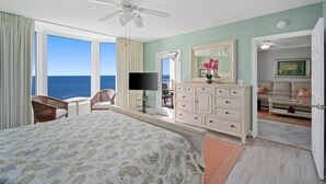 A bedroom with a bed, a ceiling fan, a TV, a dresser, and a view of the ocean. - Emerald Beach 2325 (Panama City Beach)