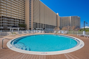 A large outdoor swimming pool surrounded by a wooden deck, with a high-rise building in the background. - Laketown Wharf 1331 (Panama City Beach)