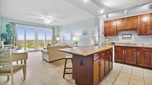 A spacious kitchen with wooden cabinets, a large island, and a dining area with a view. - Laketown Wharf 1331 (Panama City Beach)