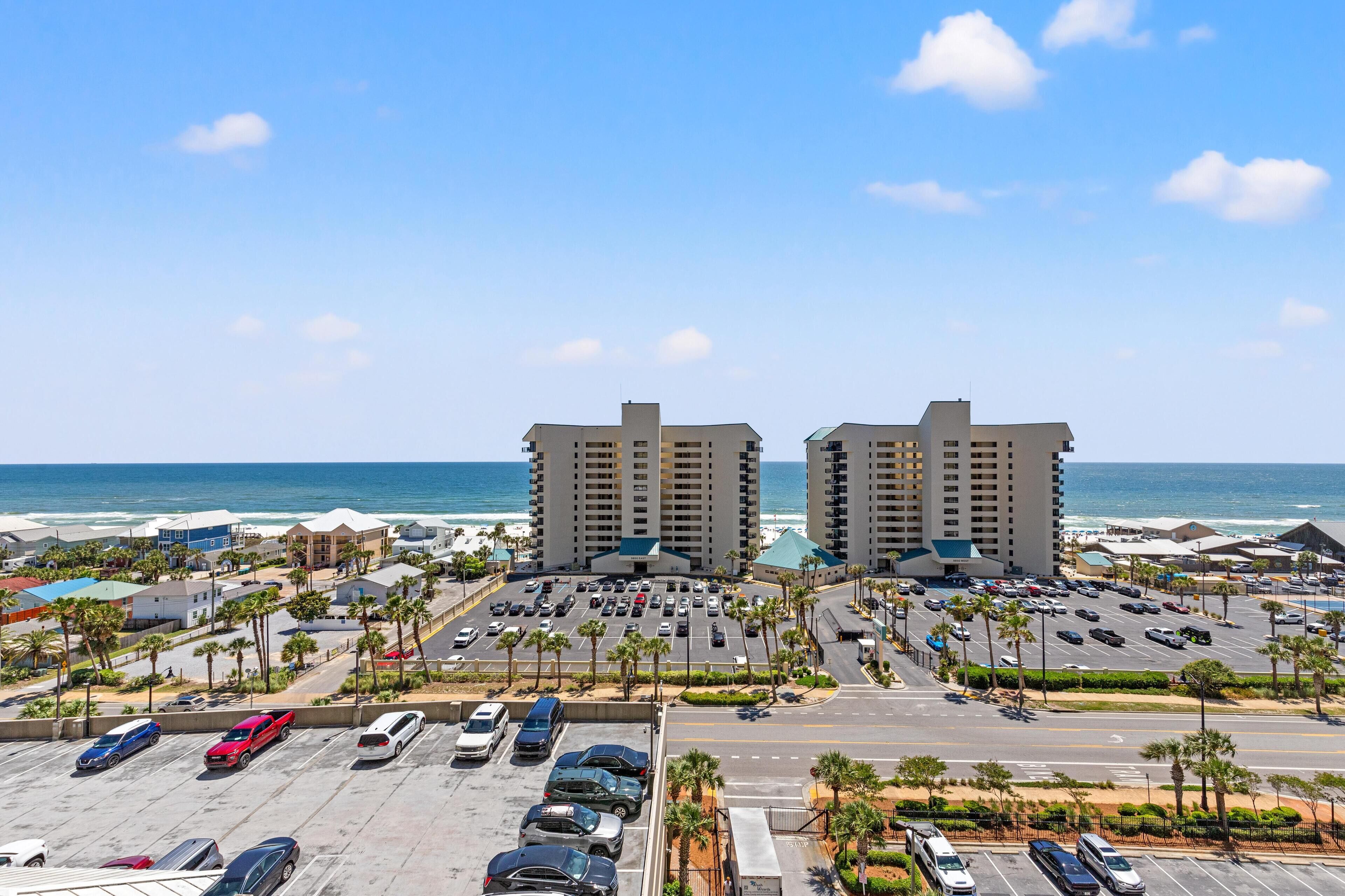 A coastal hotel with a parking lot, beachfront view, and multiple buildings.
