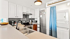 A modern kitchen with white cabinets, stainless steel appliances, and a blue curtain. - Seychelles 1006 (Panama City Beach)
