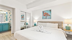A hotel room with a large bed, a bathroom with a mirror and a sink, and a painting of a flamingo on the wall. - Seychelles 1006 (Panama City Beach)