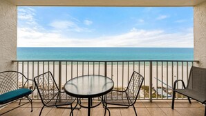 Ein Balkon mit Tisch und Stühlen, der Blick auf einen Strand mit dem Meer und einem klaren Himmel bietet.