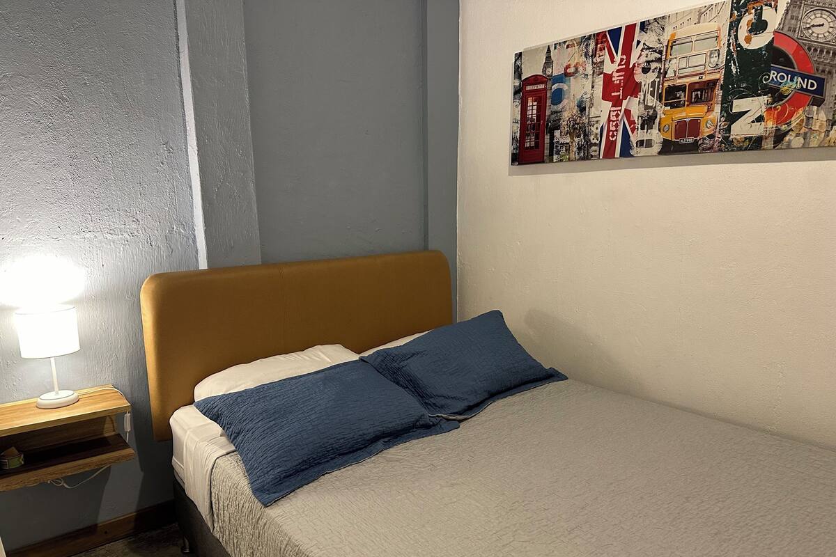 Un lit simple avec une tête de lit, une table de chevet avec une lampe et un mur orné d’une affiche.