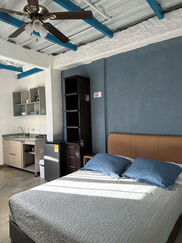 Un dormitorio con cama, ventilador de techo, escritorio y armario.