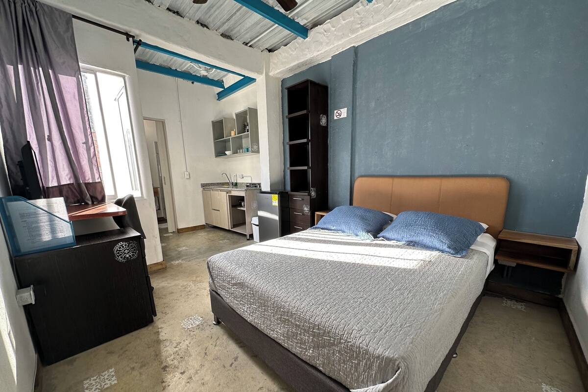 Une chambre comprenant un lit, un bureau, une armoire et un coin cuisine.