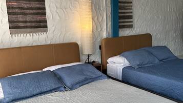 Una habitación con dos camas, cada una con cabecera y almohadas, una pared con textura y un techo con vigas azules.