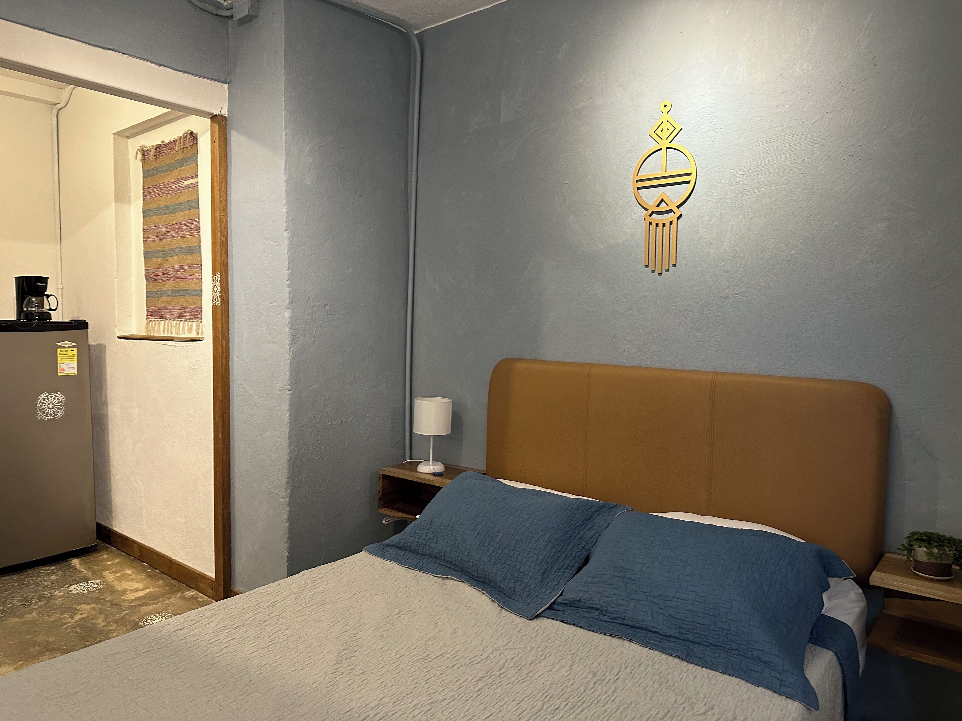 Un dormitorio con cama, mesita de noche, lámpara, decoración de pared y puerta que da a otra habitación.