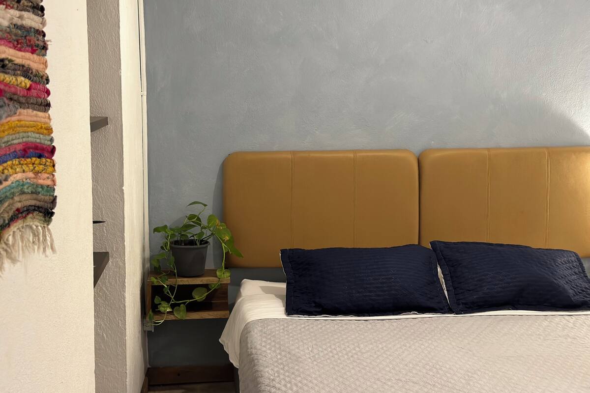 Une chambre à coucher avec un lit, une tête de lit, une table de chevet ornée d’une plante et un mur à texture.