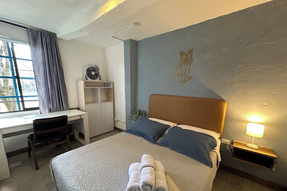 Une chambre d’hôtel comprenant un lit, un bureau, une chaise, une armoire, une œuvre d’art murale et une table de chevet avec une lampe.
