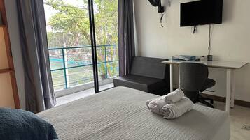 Habitación de hotel con una cama grande, un escritorio, una silla, un televisor y un balcón con vistas a zonas verdes.