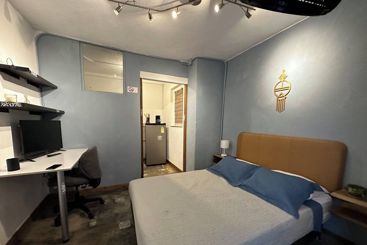 Une chambre d’hôtel équipée d’un lit, d’un bureau avec un ordinateur, d’une télévision et d’un petit réfrigérateur.