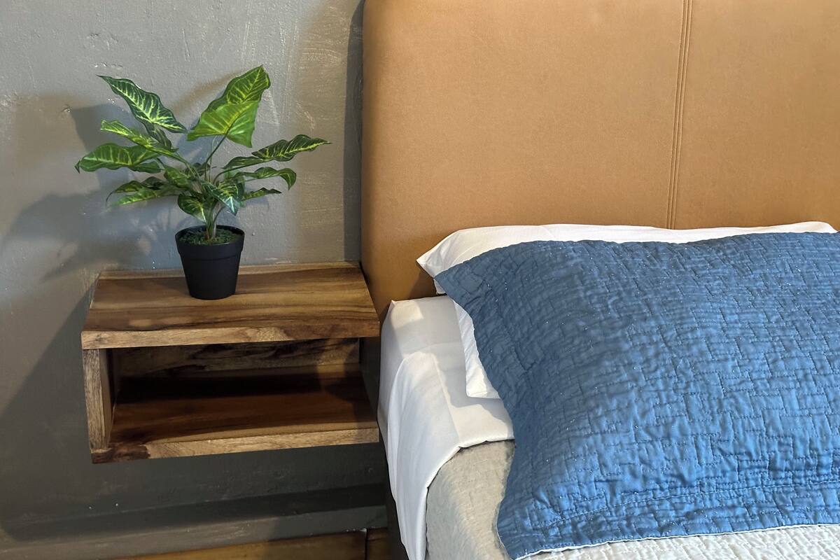 Un lit avec une tête de lit marron, une courtepointe bleue et une table de chevet en bois sur laquelle est posée une plante en pot.
