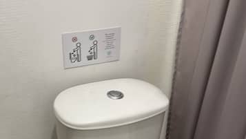 Un inodoro blanco con la tapa cerrada, un cubo de basura y un letrero en la pared con el símbolo de prohibido fumar y un icono de cubo de basura.