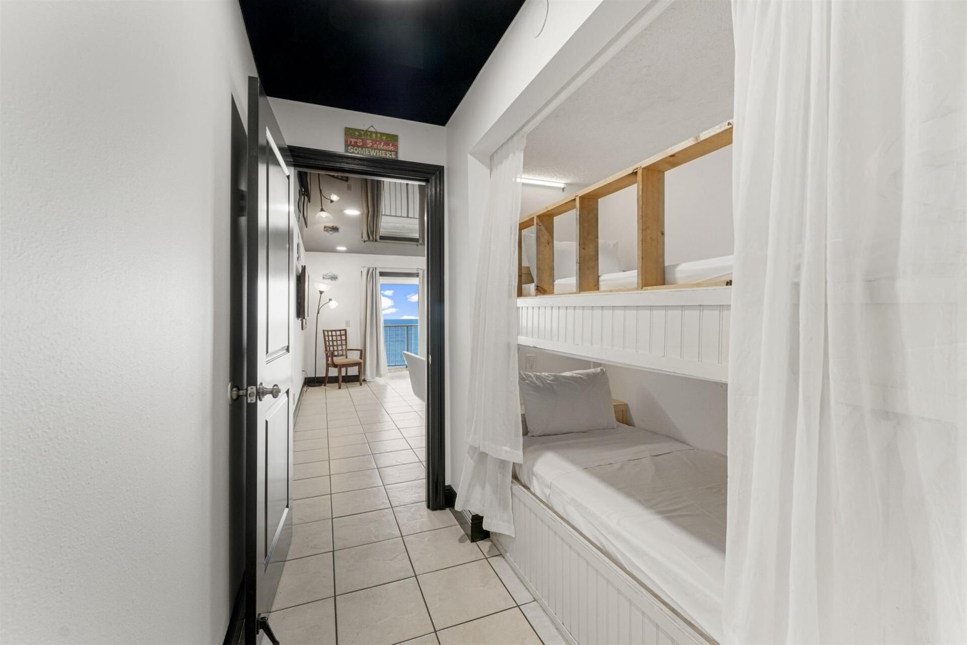 A corridor leading to a room with bunk beds, a chair, and a view of the sea.