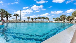 Ein Swimmingpool mit klarem, blauem Wasser, umgeben von Palmen und Liegestühlen.