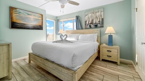 Ein Schlafzimmer mit einem hölzernen Bett, einem Deckenventilator, einem Nachttisch mit Lampe und Kunstwerken an den Wänden.