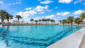 A swimming pool with clear blue water, surrounded by palm trees and lounge chairs. - The Summit 1032 (Panama City Beach)