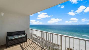 A balcony with a view of the ocean, a wooden bench, and a railing.
