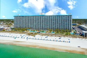 A large hotel with a modern design, located near a beach with numerous sun loungers and umbrellas. - The Summit 1216 (Panama City Beach)