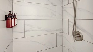 A bathroom with white marble tiles, a handheld showerhead, and a soap dispenser mounted on the wall. - Plush King Bed Xtra Clean Stay
 (Canal Point)
