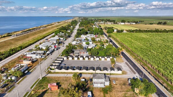 An aerial view of a coastal town with a marina, residential buildings, and agricultural fields.