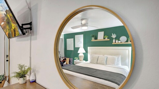 A bedroom with a large round mirror, a bed with white bedding, a ceiling fan, and a green accent wall. - Plush King Bed Xtra Clean Stay
 (Canal Point)