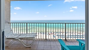 A balcony with a view of a beach, a metal bench, and a turquoise chair. - The Summit 1512 (Panama City Beach)