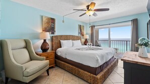A hotel room with a bed, a chair, a desk, a ceiling fan, and a view of the ocean. - The Summit 1512 (Panama City Beach)