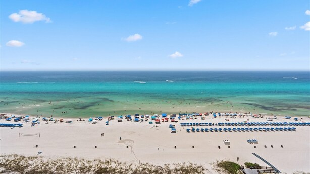 A beach with rows of blue umbrellas and beach chairs, a volleyball net, and a clear view of the ocean. - The Summit 1512 (Panama City Beach)