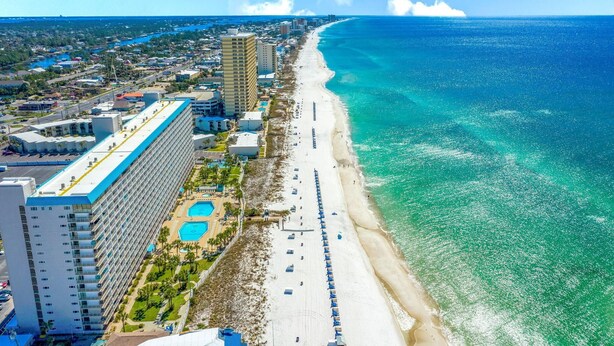 A coastal hotel with a long beachfront, multiple swimming pools, and a large building with a blue roof.