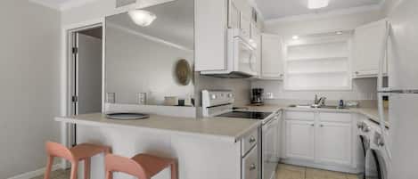 A modern kitchen with white cabinets, a central island with stools, a built-in oven, microwave, and a washing machine.
