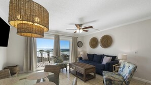 A living room with a sofa, chairs, a coffee table, a ceiling fan, and a view of the ocean.
