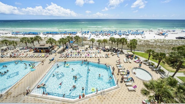 Ein Strandhotel mit mehreren Schwimmbecken, Strandsonnenschirmen und Palmen.