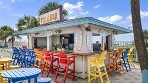 Eine Tiki-Bar mit bunten Stühlen und Tischen, einer Speisekarte und Blick auf das Meer.