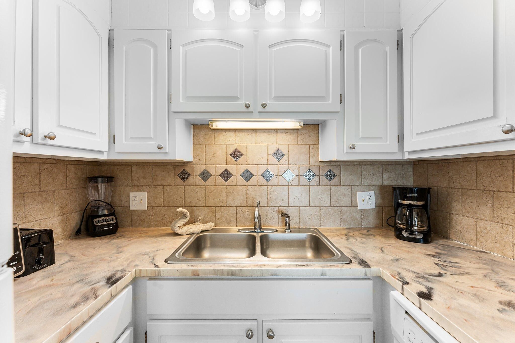 A kitchen with white cabinets, a double sink, a blender, a coffee maker, and a toaster.