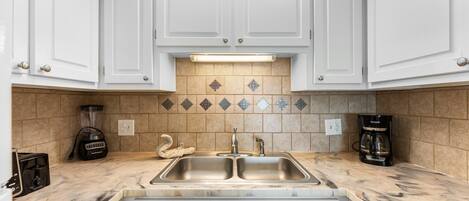 A kitchen with white cabinets, a double sink, a blender, a coffee maker, and a toaster.