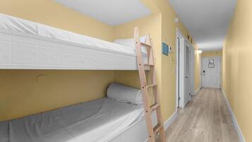 Una habitación con una cama litera, una escalera de madera, una puerta blanca y un pasillo con suelo de color claro.