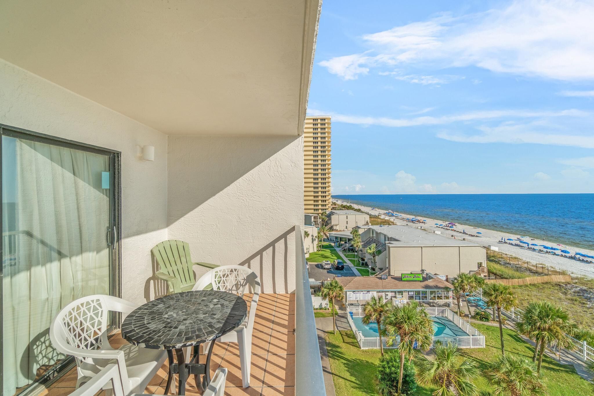 Een balkon met uitzicht op het strand en de oceaan, met een tafel en stoelen, en een zwembadgedeelte op de achtergrond.