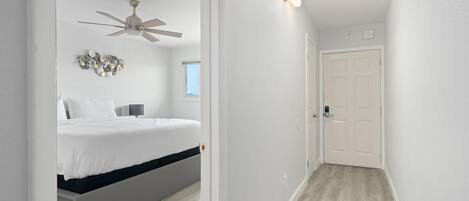 Quarto com cama, ventoinha no teto, mesa de cabeceira e luminária fixada na parede.