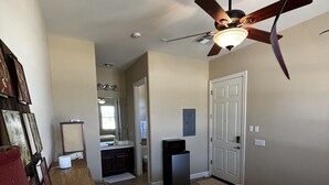 A bedroom with a bed, a ceiling fan, a heater, a door, and a small trash bin.