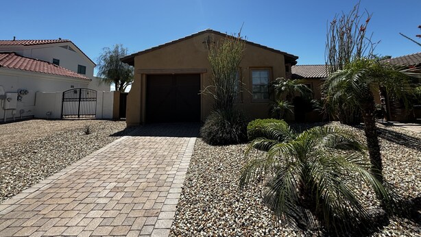A house with a paved driveway, a garage, and a garden with palm trees and shrubs.
