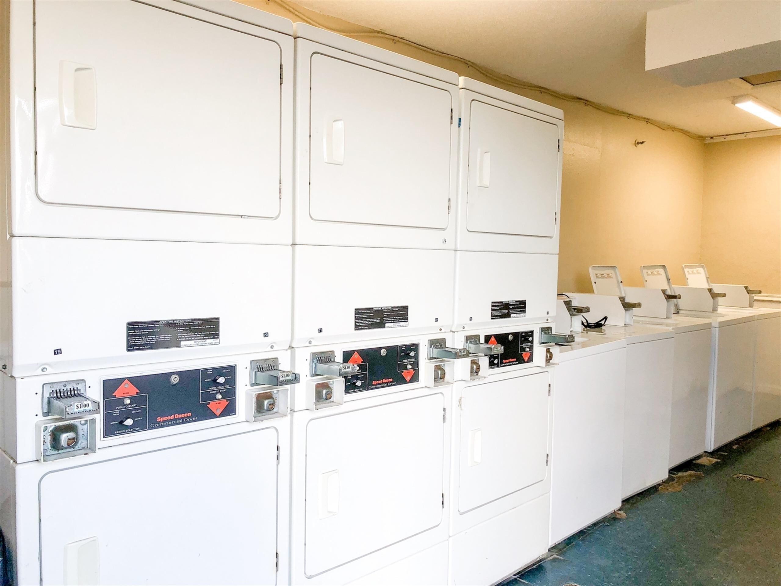 A row of white commercial dryers with control panels and safety labels.