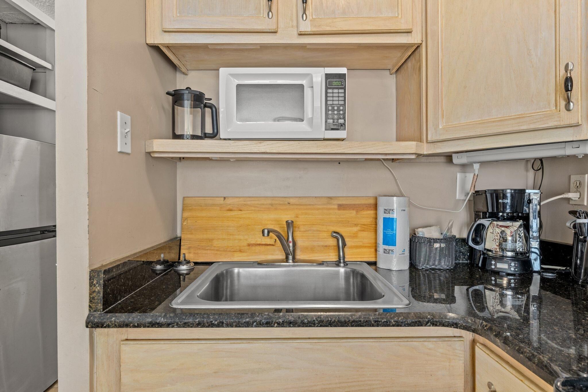 A kitchen with a stainless steel sink, a microwave, and wooden cabinets.