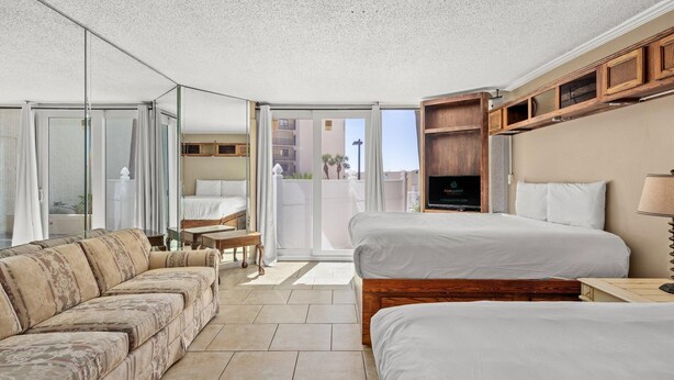 Ein Hotelzimmer mit einer Couch, zwei Betten, einem Fernseher und einer Glastür zum Balkon.