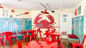 Ein Restaurantinnenraum mit roten Tischen und Stühlen, einem großen Wandgemälde mit Krebsen und einer rustikalen Holztresen.