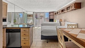 Ein kleines Hotelzimmer mit Bett, Esstisch, integriertem Geschirrspüler und großem Spiegel.